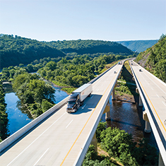 Large bridge with a semi truck and other cars driving that is crossing a body of water.